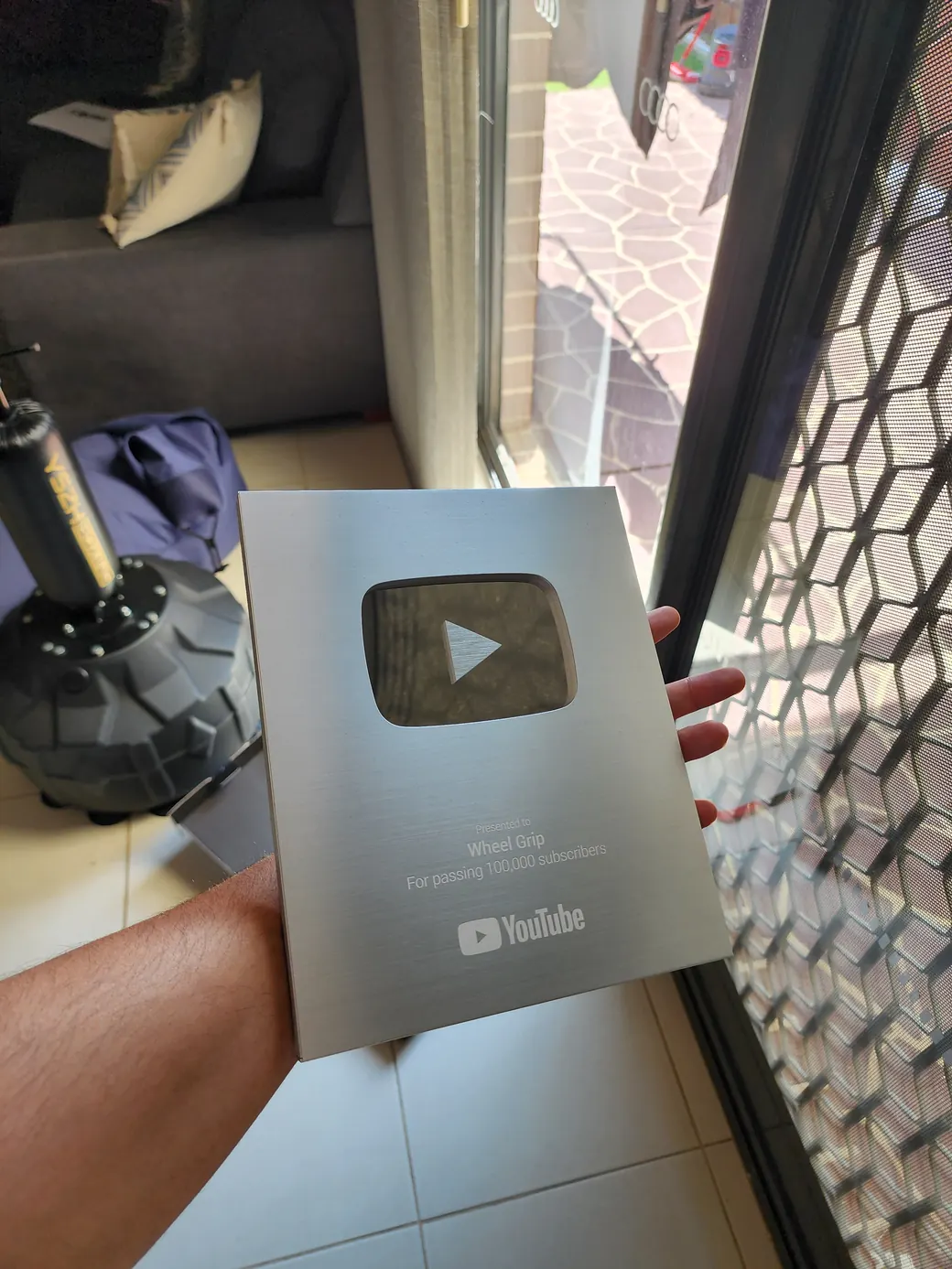 A YouTube silver play button award engraved for Wheel Grip, held in one hand